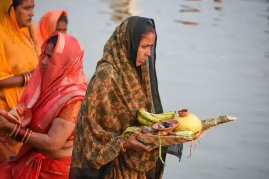 Chhath puja vrat katha: घाट पर पानी में खड़ी व्रती, हाथ में फलों से भरा सूप
