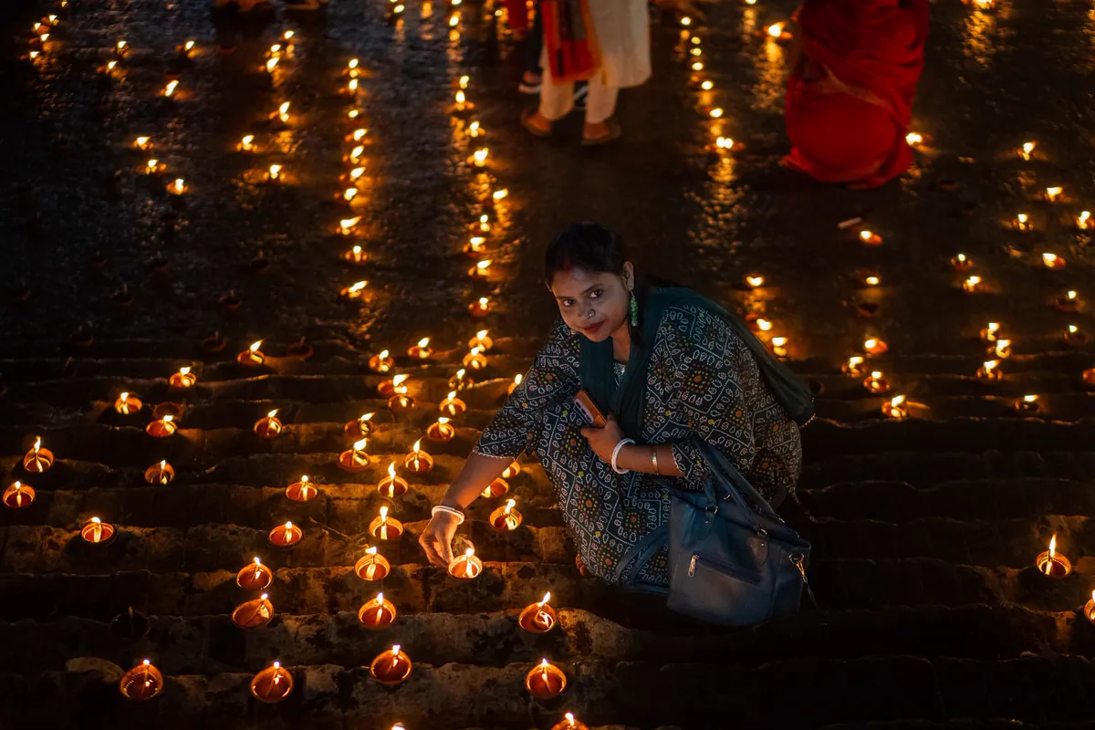 कार्तिक पूर्णिमा 2026 कब है: 24 नवंबर, स्नान दान का समय, देव दीपावली, दीपदान विधि और कथा घाट पर ज़मीन पर सैकड़ों दीये जलाती महिला