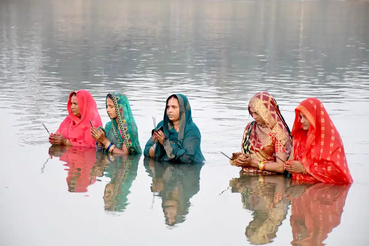 छठ पूजा 2026: व्रत कथा, चारों दिन की पूजा विधि, सामग्री सूची और ठेकुआ सुबह की धुंध में पानी में खड़ी होकर पूजा करती व्रतियाँ