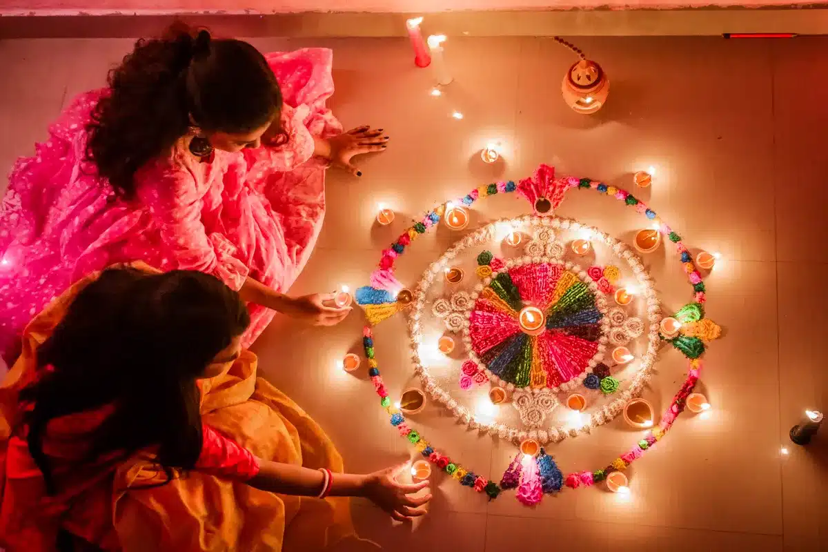 दिवाली लक्ष्मी पूजा विधि 2026: घर पर पूजा कैसे करें, कथा और सामग्री सूची रंगोली के चारों ओर दीये सजाती लड़कियाँ