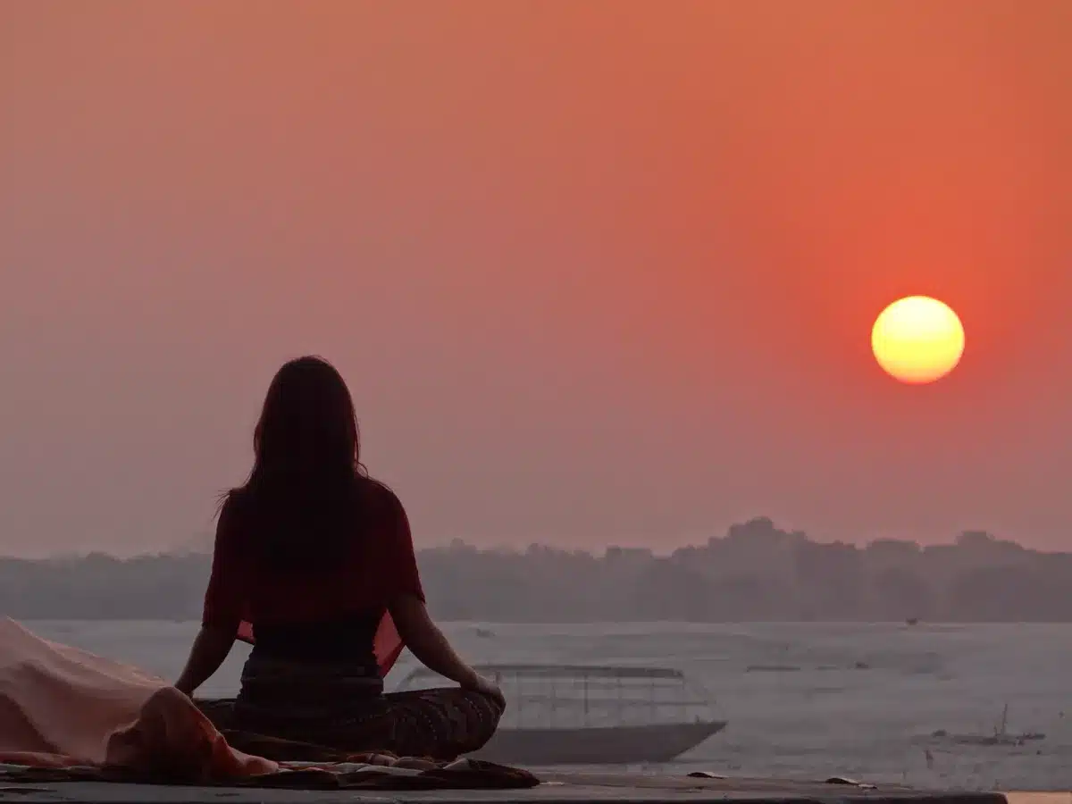 The Secret Book Summary in Hindi by Rhonda Byrne नदी किनारे सूर्यास्त के समय ध्यान करती एक महिला